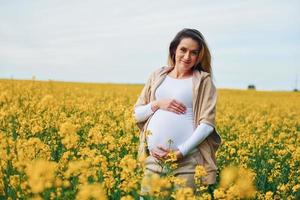 gravid kvinna Framställ på en fält av gul blommor foto