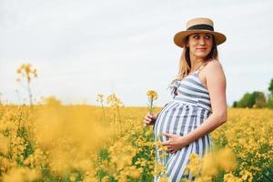 gravid kvinna Framställ på en fält av gul blommor foto