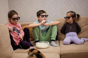 tre barn Sammanträde på de levande rum, ha på sig 3d glasögon tittar på film eller tecknad serie. foto