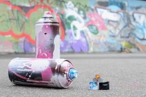 flera Begagnade spray burkar med rosa och vit måla och caps för besprutning måla under tryck är lögner på de asfalt nära de målad vägg i färgad graffiti ritningar foto