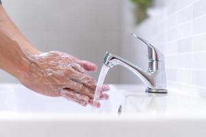 män tvättning händer med tvål och rena vatten i främre av de badrum handfat till förhindra de spridning av bakterier. tvättning händer med tvål. foto
