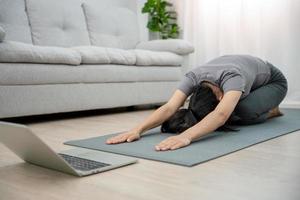 asiatisk kvinna håller på med yoga i de levande rum. yoga till håll och lossa sträckor till minska tillbaka smärta. Lycklig till övning foto