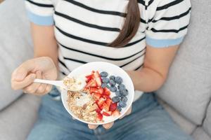 kvinna har utsökt friska frukost på Hem på morgon. hälsa vård kvinna äter yoghurt med granola och bär frukt. friska mat, vitaminer, rena diet, bantning, detox, vegetarian, organisk mat. foto