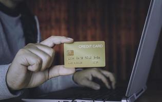 man innehav kreditera kort till betalande och använder sig av bärbar dator till uppkopplad handla på Hem. mest människor använda sig av mobil bank till betalning begrepp. foto