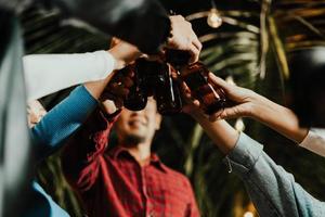 grupp asiatisk människor Lycklig vänner fira och klirr med flaskor av öl foto