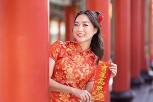 asiatisk kvinna i röd Cheongsam qipao klänning är innehav välsignelse förmögenhet kort ordspråk 'till vara välsignad förbi en tur- stjärna' inuti kinesisk buddist tempel under lunar ny år för bäst önskar och Bra tur foto