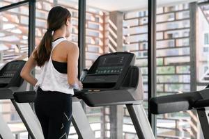 ung Lycklig asiatisk kvinna idrottare springa på löpband, löpning maskin, i inomhus- Gym kondition för hälsa foto