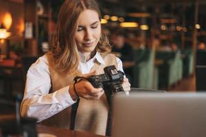 ung kvinna fotograf arbetssätt med henne kamera med bärbar dator i en Kafé foto