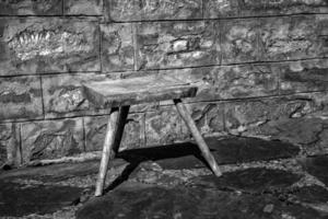 gammal små trä- stol i de lantlig gård nära en sten vägg. svart och vit foto