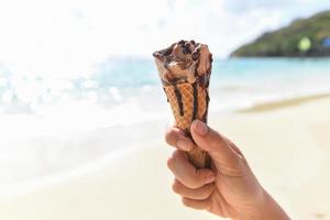 is grädde kon i hand med hav bakgrund - smältande is grädde på strand i sommar varm väder hav landskap natur utomhus- semester , is grädde choklad foto