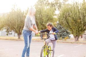 mor undervisning henne liten dotter på vilket sätt till rida en cykel foto