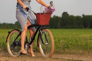 kvinna i blå klänning ridning på en svart cykel i en sommar fält foto