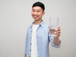 positiv asiatisk man blå skjorta ger glas av vatten till du med Lycklig leende isolerat foto