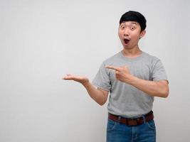 asiatisk man grå skjorta visa tömma hand upp och gest punkt finger känner förvånad på ansikte isolerat foto