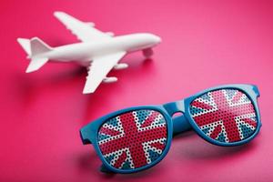 turkos solglasögon med förenad rike flagga i linser på galen rosa bakgrund med vit flygplan. t foto