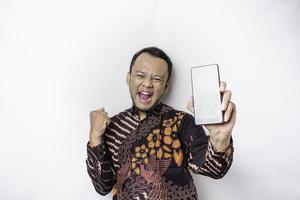 en Lycklig ung asiatisk man bär batik skjorta som visar framgångsrik uttryck som visar kopia Plats på hans telefon isolerat förbi vit bakgrund foto