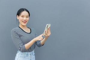 porträtt av skön asiatisk kvinnor använda sig av de smart telefon lyckligt på grå bakgrund foto