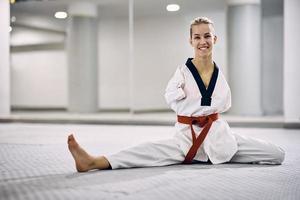 Lycklig kvinna krigisk konst idrottare med handikapp uppvärmningen upp medan utövar taekwondo i hälsa klubb. foto