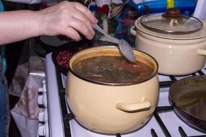 tomat soppa borscht är kokta i en metall kastrull. de kvinna rör om med en sked. foto