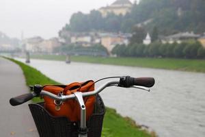 resa till salzburg, Österrike. en cykel på en se av en parkera, en flod och berg. foto