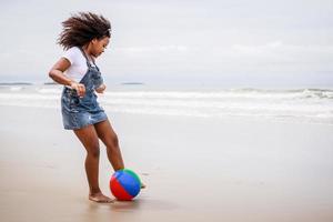 rolig semester. afrikansk amerikan unge flicka spelar boll och har roligt på en tropisk strand foto
