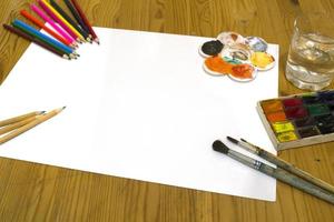 teckning förnödenheter. pennor, målar, borstar, papper och en glas av vatten på de tabell. foto