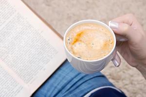 kopp av kaffe och en bok i kvinna hand foto