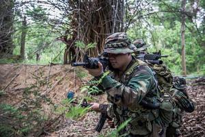 team av armésoldat med maskingevär som rör sig i skogen, thailändsk milissoldat i stridsuniformer i skogen, vandra patrullen som sluttar i regnskogen. foto