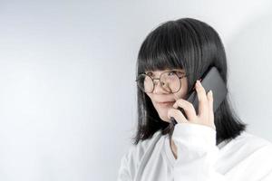 isolerat Söt asiatisk glasögon kvinna samtal och talar i de linje med henne mobil telefon på vit bakgrund i studio ljus. foto