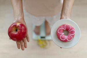 kvinnor är välja de rätt mat för Bra hälsa. kvinnor är fasta. jämförelse alternativ mellan munkar och äpplen under vikt mått på digital vågar. diet begrepp. foto