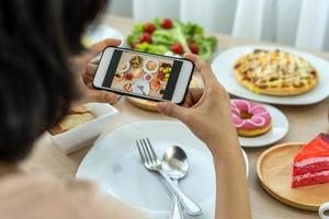 kvinnor använda sig av mobil telefoner till ta bilder av mat eller ta leva video på social nätverkande applikationer. mat för middag utseende aptitlig. fotografi och ta bild för recension mat begrepp foto