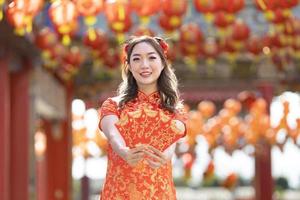 asiatisk kvinna i röd Cheongsam qipao klänning är innehav röd kuvert för pengar ordspråk Maj du ha bra tur och vinst inuti kinesisk buddist tempel under lunar ny år för bäst önskar välsignelse begrepp foto