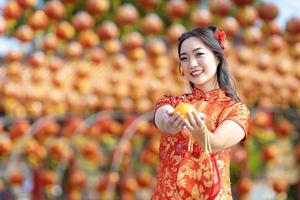 asiatisk kvinna i röd Cheongsam qipao klänning är erbjudande mandarin till de förfäder Gud inuti kinesisk buddist tempel under lunar ny år för bäst önskar välsignelse och Bra tur begrepp foto