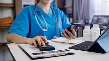 sjukvårdskostnader och avgifter concept.hand av smart läkare använde en miniräknare och smartphone, surfplatta för medicinska kostnader på sjukhus i morgonljus foto