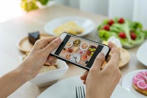 kvinnor använda sig av mobil telefoner till ta bilder av mat eller ta leva video på social nätverkande applikationer. mat för middag utseende aptitlig. fotografi och ta bild för recension mat begrepp foto