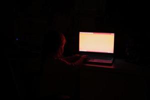 bebis flicka kran på bärbar dator medan Kolla på på färgad skärm i ljus av rum. foto