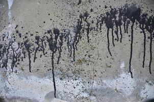 en fotografera av en närbild av svart måla fläckar på en betong vägg. häller måla på de vägg i slumpmässig ordning. de begrepp av graffiti och gata konst kultur foto