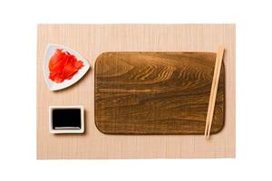 tömma rektangulär brun trä- tallrik med ätpinnar för sushi, ingefära och soja sås på brun sushi matta bakgrund. topp se med kopia Plats för du design foto