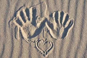 hand skriva ut med hjärta i de sand på de strand. vågig sand. fortfarande liv på de havsstrand foto