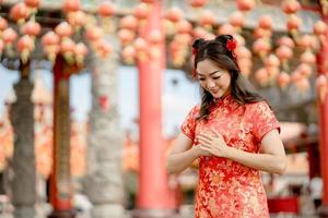 Lycklig kinesisk ny år. skön lady bär traditionell Cheongsam qipao klänning med gest av congratulation i kinesisk buddist tempel. foto