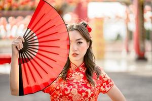 Lycklig lunar kinesisk ny år festival. ung lady bär traditionell Cheongsam qipao kostym innehav fläkt i kinesisk buddist tempel. foto