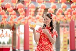 Lycklig kinesisk ny år. asiatisk kvinna bär traditionell Cheongsam qipao klänning innehav och pekande till gammal guld pengar i kinesisk buddist tempel. fira kinesisk lunar ny år. foto