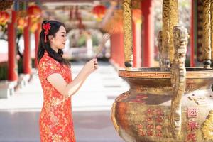 skön asiatisk kvinna bär traditionell Cheongsam qipao klänning bön- med rökelse pinnar under kinesisk eller lunar ny år, kinesisk ny år foto