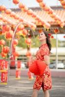 vertikal bild. Lycklig asiatisk kvinna bär traditionell Cheongsam qipao klänning innehav lykta medan besöker de kinesisk buddist tempel. fira kinesisk lunar ny år, festlig säsong Semester. foto
