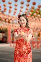 Lycklig kinesisk ny år. en ung lady bär traditionell Cheongsam qipao klänning innehav gammal guld pengar och väska i kinesisk buddist tempel. fira kinesisk lunar ny år. foto