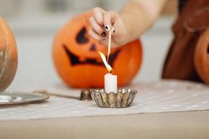 barn flicka tänder ett ljus för halloween. liten flicka i häxdräkt med carving pumpa med ett ansikte gjort av barn. lycklig familj förbereder sig för halloween. selektiv fokusering foto