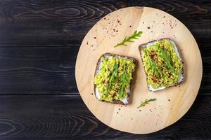 uppsättning smörgåsar för frukost - skiva av hela spannmål mörk bröd, grädde ost, guakomole, garnerad med ruccola, paprika på trä- tabell topp se platt lägga friska mat begrepp hemlagad foto