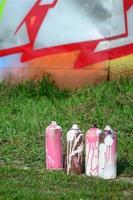 en få Begagnade måla burkar lögn på de jord nära de vägg med en skön graffiti målning. gata konst och vandalism begrepp foto