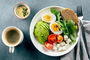 friska vegan frukost skål. avokado, ägg, tomat, fetaost ost, arugula och bröd och kopp av kaffe. topp se foto