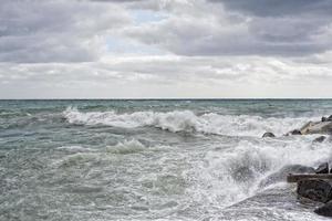 hav i storm på stenar av italiensk by foto